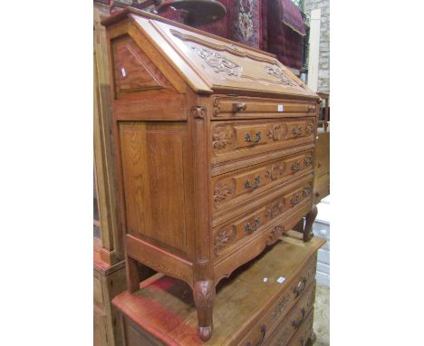 A medium to light oak bureau with fall flap over three long drawers with carved and moulded detail raised on squat scrolled c