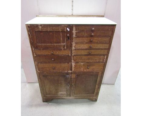 A vintage dentists cabinet freestanding and enclosed by an arrangement of drawers and cupboards beneath a green panelled top 