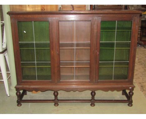 An oak side cabinet, freestanding and enclosed by three leaded light panelled doors, two with green tinted glass revealing ad