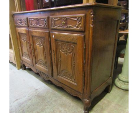A medium to light oak dresser enclosed by three rectangular panelled doors and three frieze drawers with carved detail over a