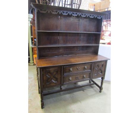 An Edwardian/1920s oak dresser, the base partially enclosed by a pair of geometric moulded panelled doors flanking two long d