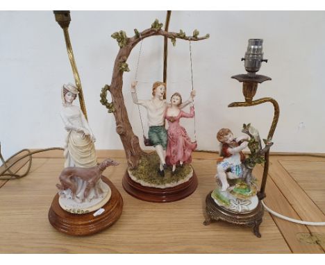 A table lamp with a bisque model of a boy and girl on a swing, and two other figural table lamps, all with shades (3).