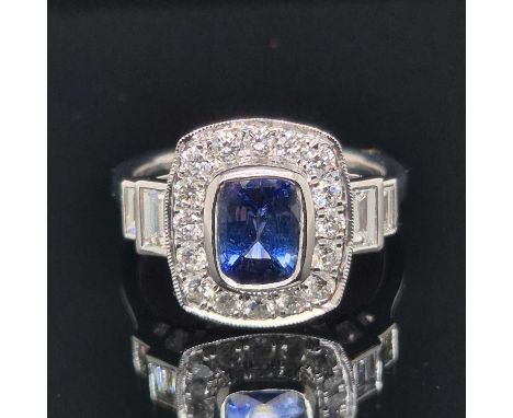 A hallmarked platinum Art Deco style sapphire and diamond ring. The central cushion cut sapphire is surrounded by round brill
