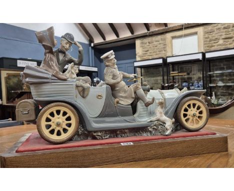A Lladro vintage car carrying parents and two children, the foot of the chauffeur being greeted by a dog as he prepares to ge