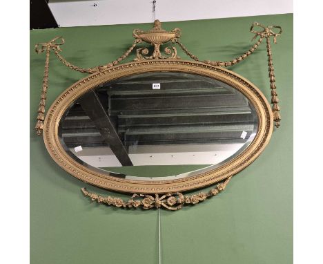 A bevelled glass oval mirror in a gilt egg and dart bordered frame crested by an urn and garrya swags.   84 x 104cms
