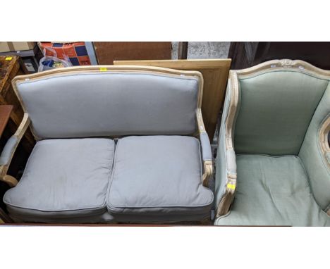 A French style limed wood framed two seater sofa and matching armchair, upholstered loose cushion seats, backs, and armrests,