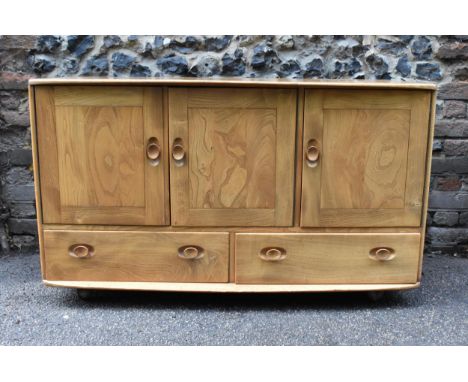 A mid century blonde elm Windsor sideboard by Ercol, with twin cupboard doors enclosing a shelf, flanked with a single cupboa