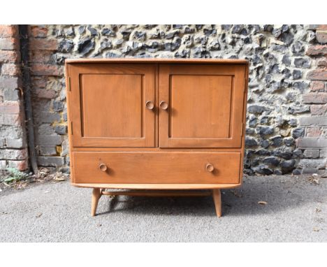 A mid century light ash sideboard in the Ercol style, with twin cupboard doors enclosing a shelf above a bottom frieze drawer