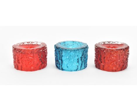 Three Whitefriars glass 'Bark Effect' candle holders designed by Geoffrey Baxter, pattern 9733, comprising two ruby red and a