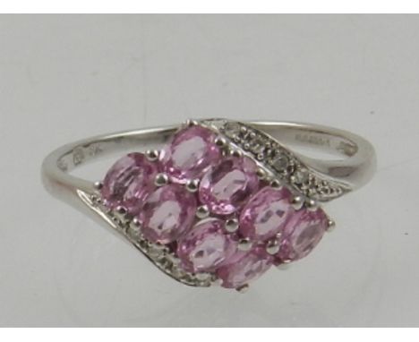 A 9 carat white gold, pink sapphire, and diamond crossover ring, set eight oval cut sapphires, flanked by eight diamond accen