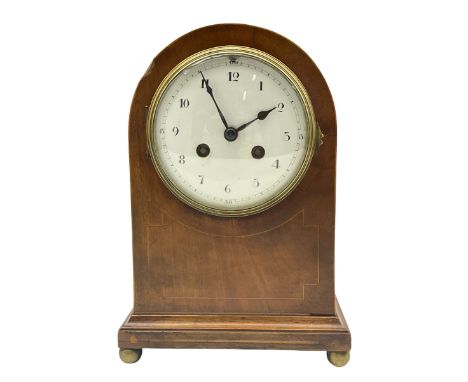 An Edwardian mantle clock in an arched mahogany case inlaid with satinwood stringing on a moulded plinth with ball feet (one 