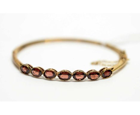 A Victorian style garnet bangle, the seven oval facet cut garnets on plain 9ct yellow gold bangle, 6cms wide, 10.4g gross,