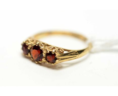 A three stone garnet ring, the circular facet cut graduated garnet in scrolling mount and 9ct yellow gold shank, ring size N.