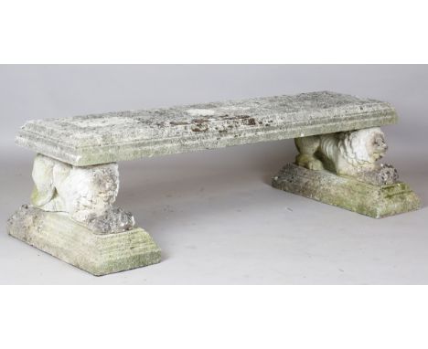 A 20th century cast composition stone rectangular garden bench, raised on a pair of recumbent lion supports and plinth bases,