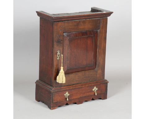 An 18th century provincial oak spice cupboard, the hinged door inset with a mahogany panel, enclosing an arrangement of drawe