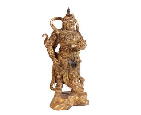 BRONZE WARRIOR FIGURE OF THE GUARDIAN KING DHANADAR, QING DYNASTY, depicted as the warrior standing on a rockwork base, weari