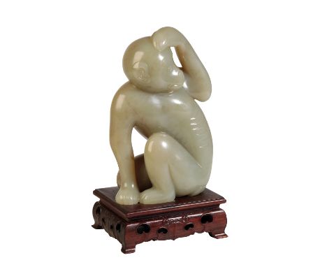 LARGE CARVED CELADON JADE MONKEY, REPUBLIC PERIOD OR LATER, modelled seated with one arm raised over its head, on a hardwood 