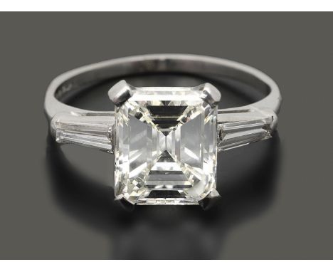 A rectangular cut-cornered single stone diamond ringthe step-cut diamond weighing 3.00cts, claw-set to either side with a tap