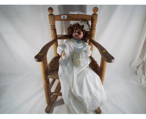 A good quality wood and wicker child's rocking chair with a child's doll with bisque head, glass eyes and open mouth. Head is