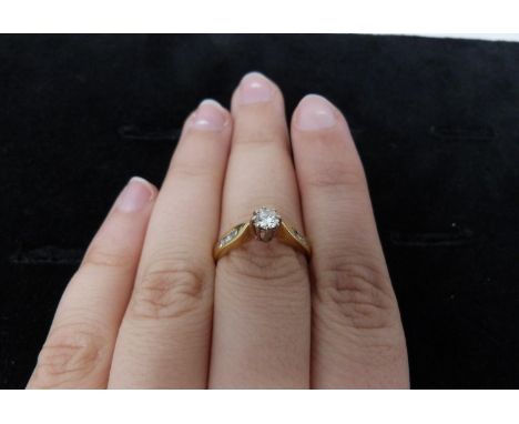 A flanked solitaire diamond ring, set to centre with a round brilliant cut diamond in a claw setting with an approximate cara