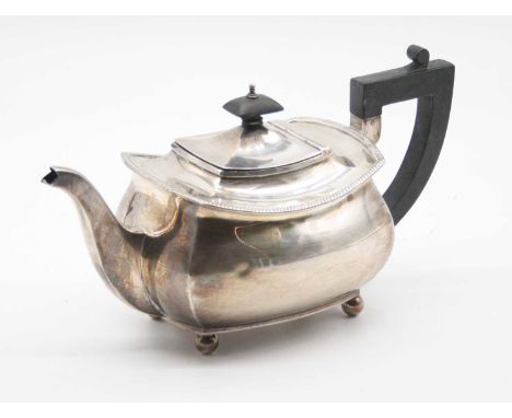 An Ewardian silver teapot of squat rectangular form having beaded rim and ebonised handle, raised on ball feet, weight 19.5oz