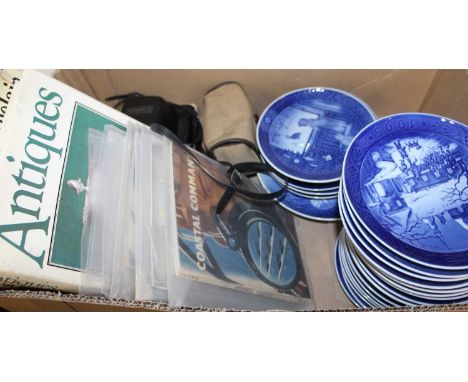 A box containing a collection of various Royal Copenhagen Christmas plates, antique reference books, and a vintage camera