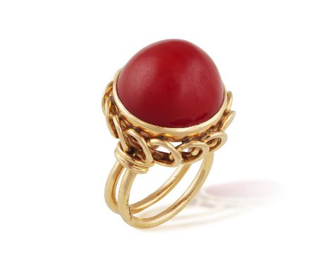 A RETRO CORAL RING, CIRCA 1960The central circular corallium rubrum cabochon, raised by looped gallery, to a bifurcated hoop,