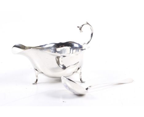 A silver sauce boat and a sauce ladle. The sauce boat with a shaped rim, flying scroll handle and three pad feet, hallmarks f