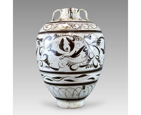 of ovoid shape rising to a narrow short neck with rolled lip,with  four stylized loop handles attached to the shoulder, and w