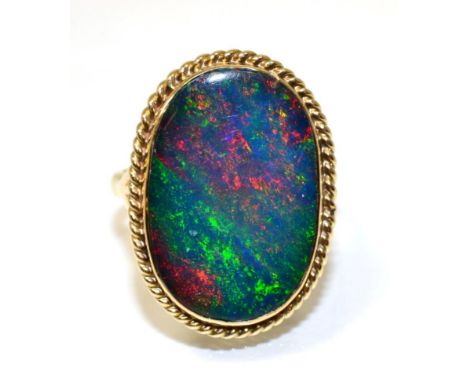 A 9 carat gold boulder opal ring, an oval cabochon opal in a rubbed over setting within a rope frame, to scroll shoulders, fi