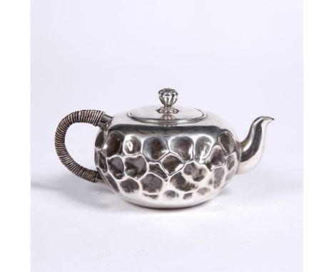 A Japanese silver teapot and cover the squat globular body decorated with irregular indentations, cover with petalled finial 