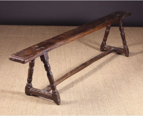 A 17th Century French Provincial Fruitwood Bench. The narrow plank seat with moulded edge pierced by the rectangular tenons o