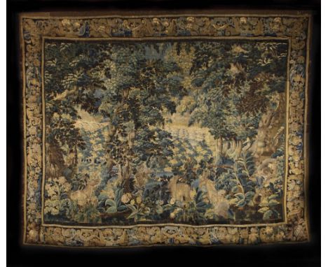 A 17th Century Tapestry depicting a woodland scene with a figure and three deer amongst the foliage, framed by a floral borde