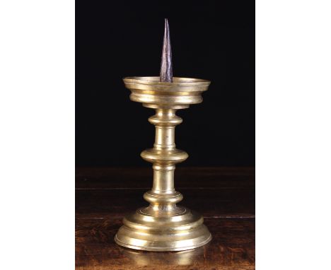 A 16th Century Flemish Gothic Brass Pricket Stick having an iron spike centring a dished drip pan above a fillet knopped cyli