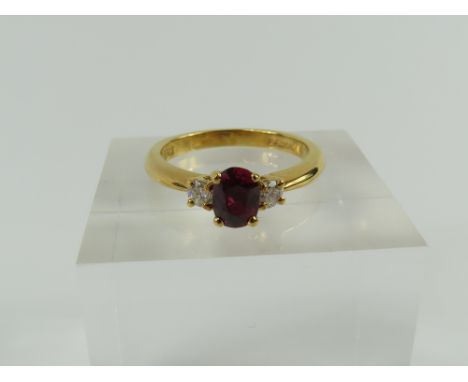 An 18ct gold ruby and diamond three stone ring, the oval cut ruby in four claw setting with a round diamond to each side, fin
