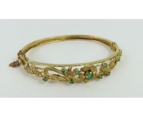 A 9ct gold emerald set bangle, the stones set into an openwork floral design, internal diameter 5.7cm, 13.38g gross