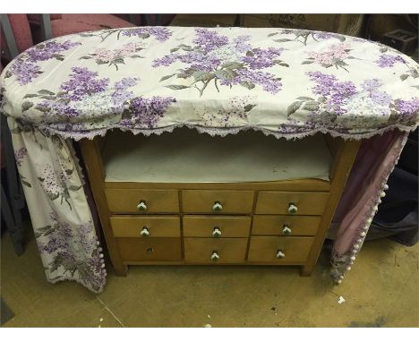 Light coloured wood kidney shaped dressing table with nine small drawers under an applied curtain