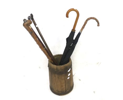 A walking stick stand and contents. The vintage stand constructed of a copper bound wood churn, containing two umbrellas and 