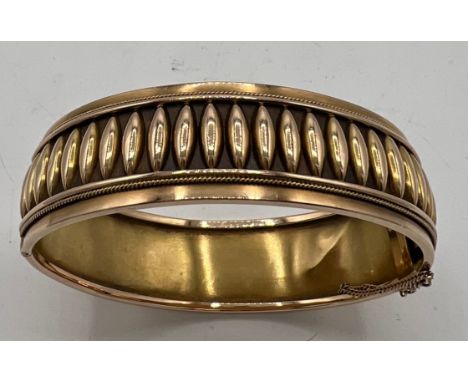 A yellow metal hinged bangle, tests as 14carat gold. Decorated to one side. 28gm weight. 