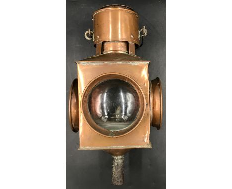 A large copper signal lamp containing four lenses, two red, two clear, one of which has concentric circles with one opening p