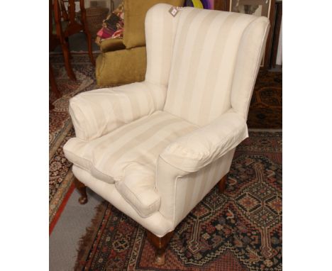 A wing armchair, upholstered in a cream fabric with loose seat cushion, on cabriole supports