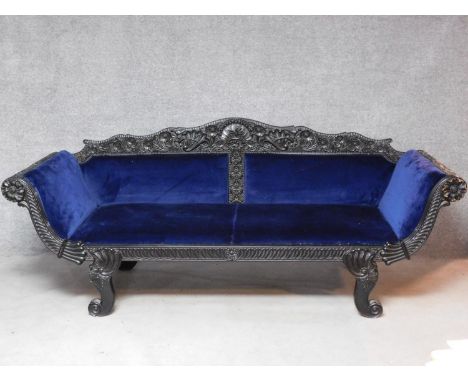 A 19th century Anglo Indian carved ebonised scroll end sofa with blue velvet upholstery on scroll swept supports. Intricately