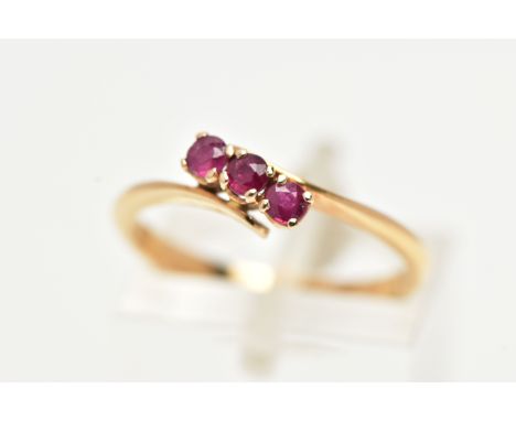 A THREE STONE RUBY RING, three circular cut rubies prong set in yellow metal, leading on to a bypass mount, stamped 18ct, rin