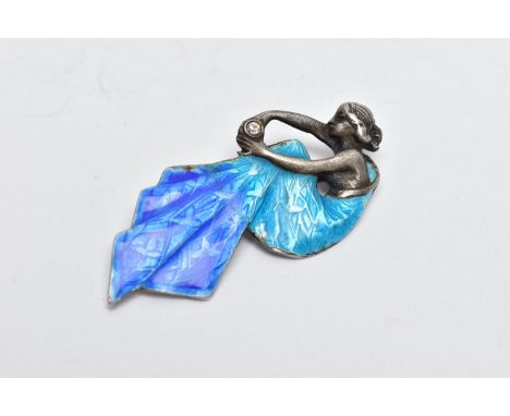 A WHITE METAL AND ENAMEL BROOCH, in the form of a seated lady holding a circular cut cubic zirconia in a bezel setting, detai