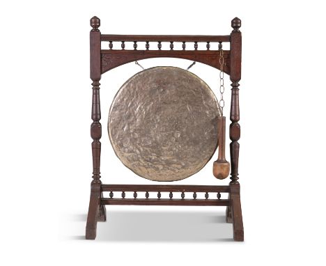 AN OAK AND BEATEN BRASS DINNER GONG, 19th century, the circular panel suspended from a turned oak stand, with hammer, on spla