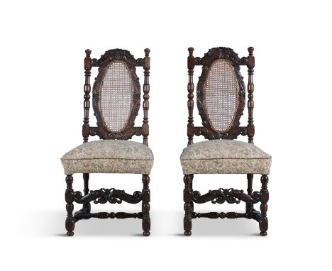 A PAIR OF WALNUT STAINED AND CARVED FRAME SIDE CHAIRS, with oval cane panel backs, the crests with foliate scrollwork, padded