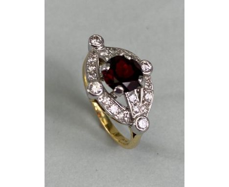 Unmarked yellow and white gold ring set with a central red faceted Gemstone in four claws and framed by an oval and cross mou