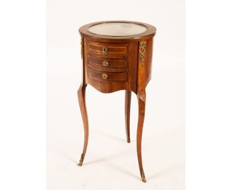 An Edwardian satinwood and inlaid circular vitrine table, the glazed top above three drawers, decorated trophy of instruments