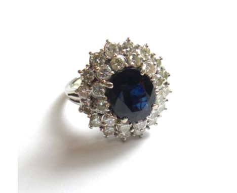 A white gold, sapphire and diamond set oval cluster ring, claw set with the oval cut sapphire at the centre, within a two row