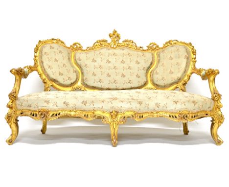 A Rococo Revival gilt framed open settee, the triple bow seat on scroll supports, 176cm wide.  Illustrated